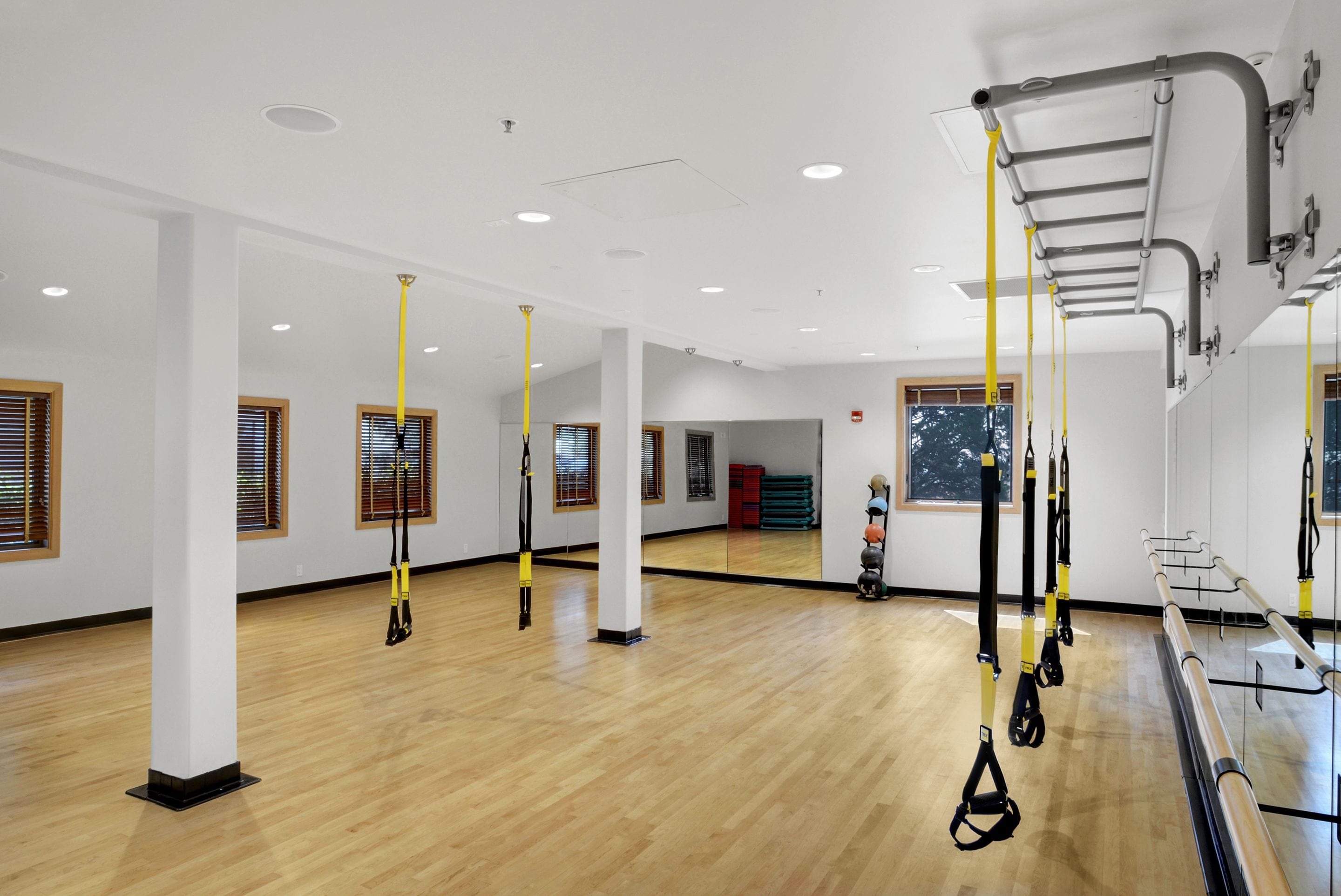 A spacious room with wooden flooring, white walls, and multiple TRX suspension straps hanging from the ceiling.