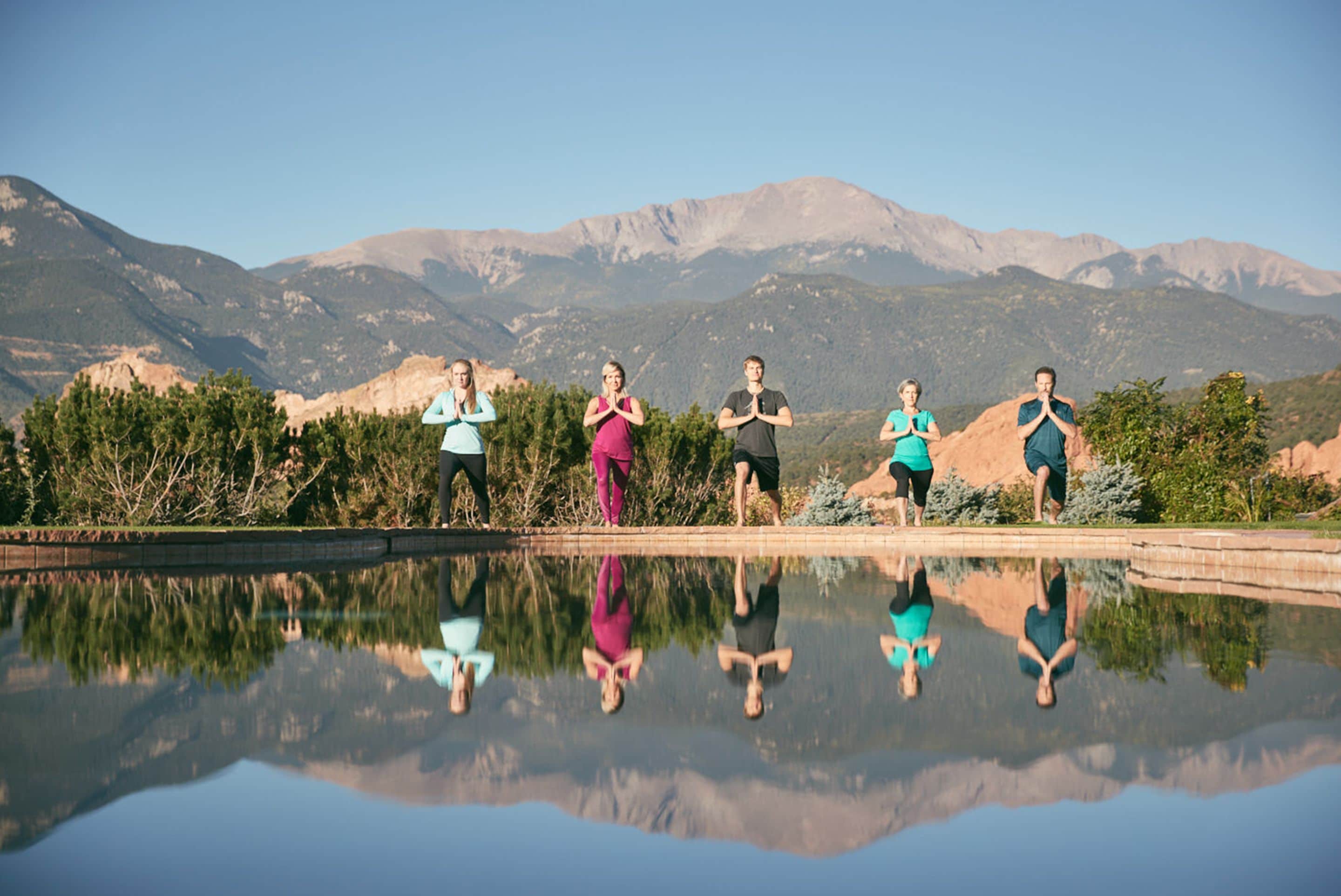 A group of people standing by a reflective pool with mountains in the background.