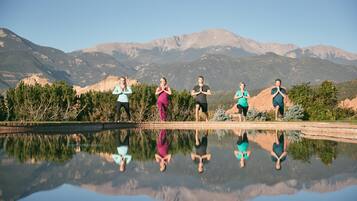 A group of people standing by a reflective pool with mountains in the background.