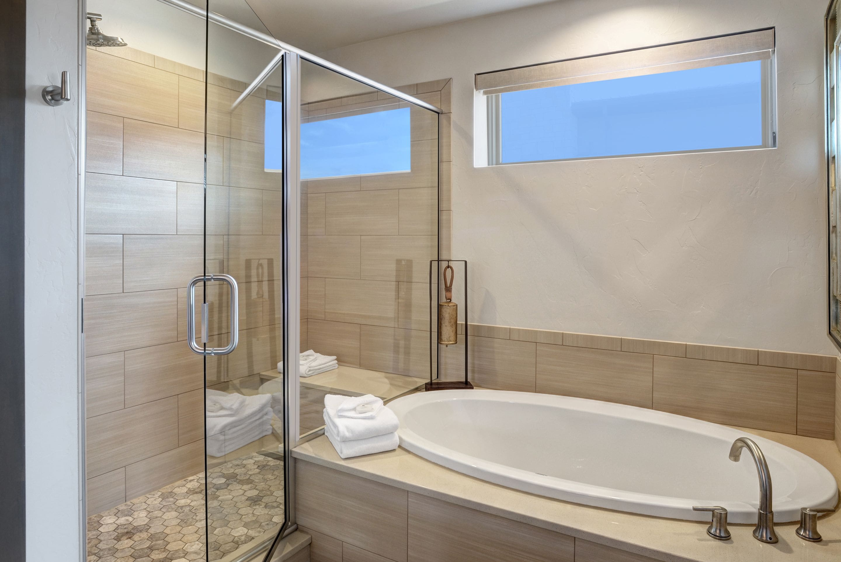 A modern bathroom with a glass-enclosed shower, a large bathtub, and a window providing natural light.