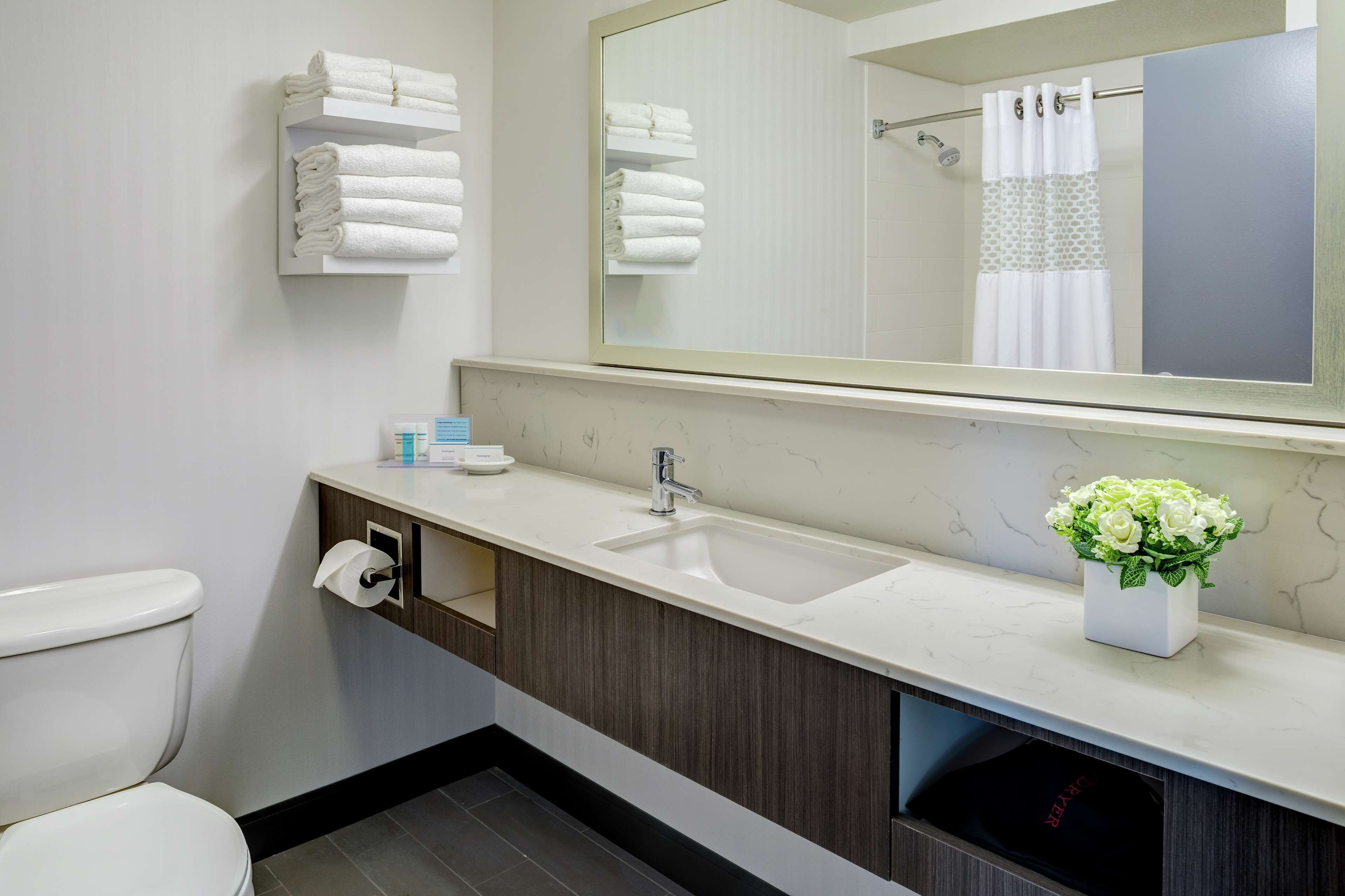 Un baño moderno con inodoro blanco, lavamanos con espejo y toallero con toallas dobladas.