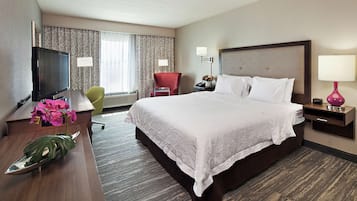 A hotel room with a large bed, a desk with a TV, a chair, and a desk lamp.