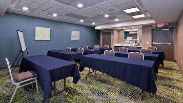 A conference room with tables and chairs, a whiteboard, and a kitchenette area.