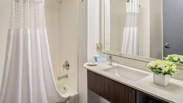 A bathroom with a shower curtain, a sink, a mirror, and a vase with flowers.