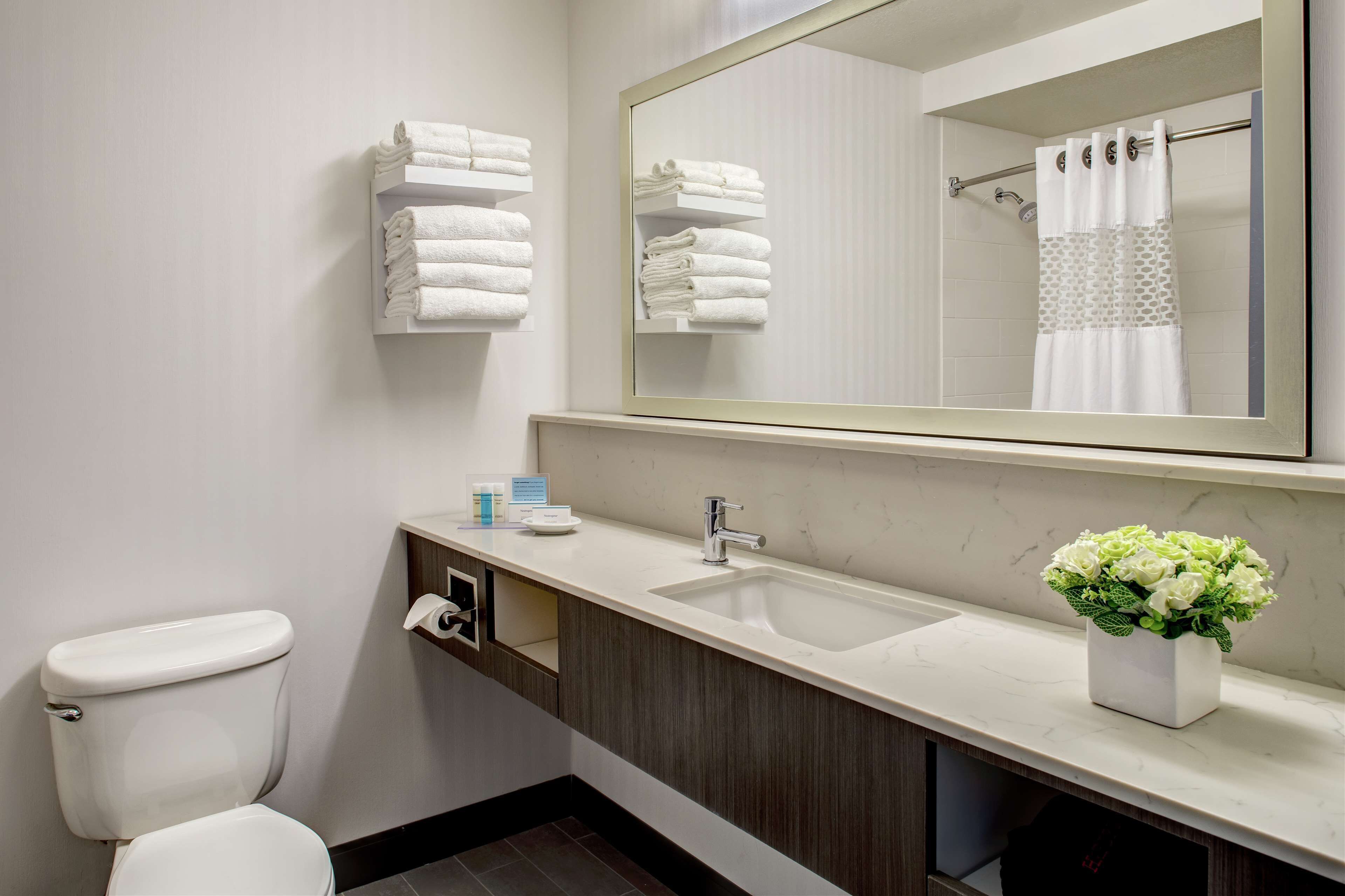 A modern bathroom with a white toilet, a sink with a mirror above it, and a towel rack with folded towels.