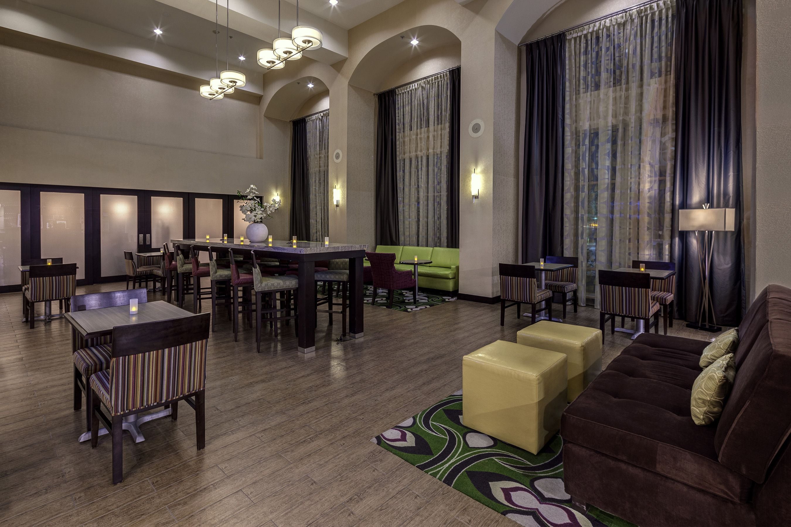 Un amplio vestíbulo de hotel con zona de comedor, arreglos de asientos y un ventanal con cortinas.