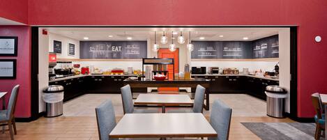 A modern restaurant with a central counter, seating area, and decorative lighting.
