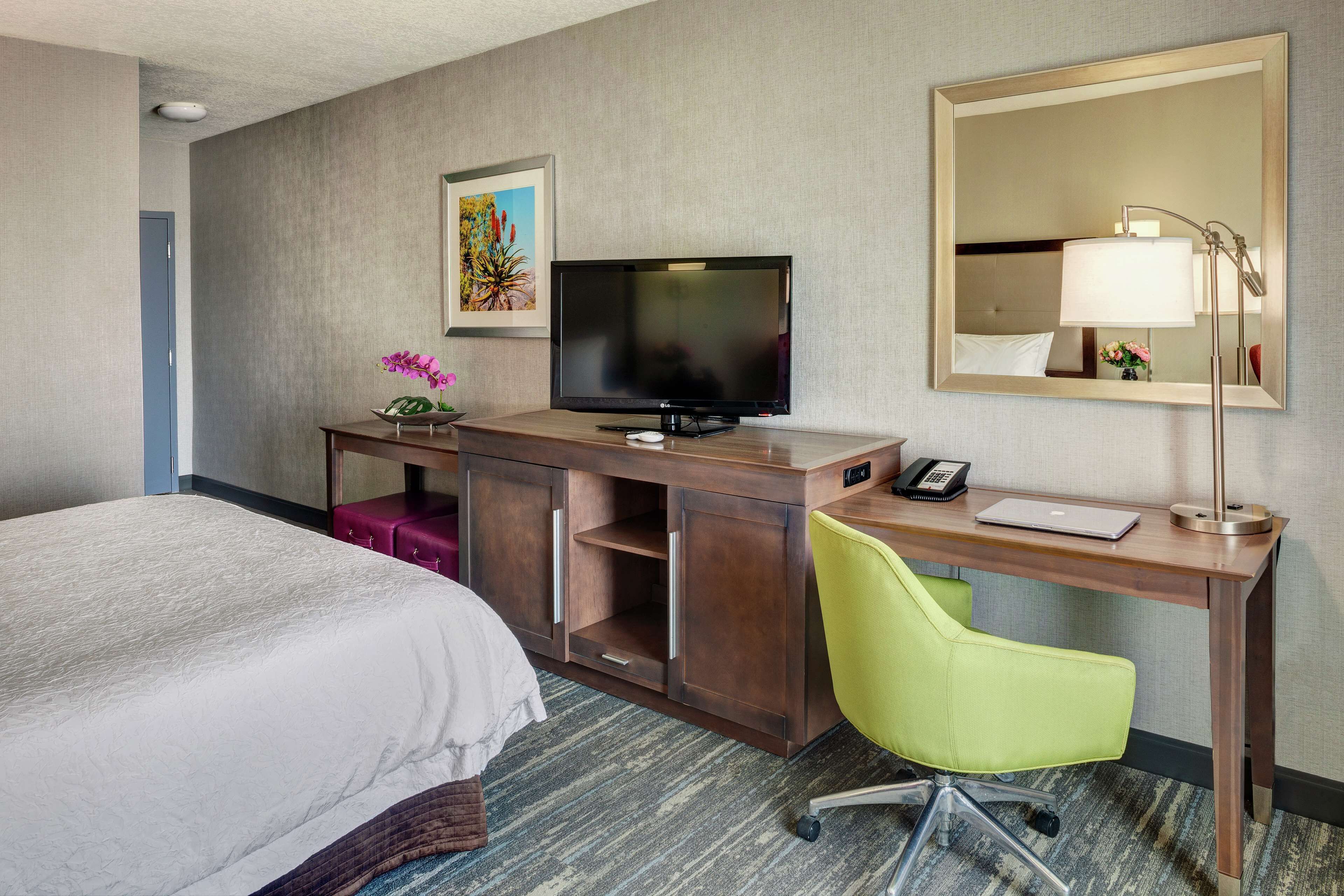 A hotel room with a bed, a desk with a computer, a television, and a mirror.