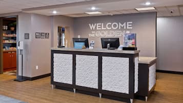 A reception desk with a 'Welcome to the Golden' sign, a digital screen, and a beverage dispenser.
