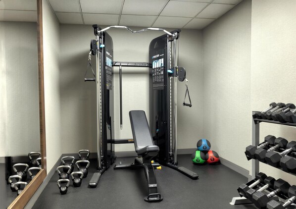 A gym with a bench press, kettlebells, and dumbbells.