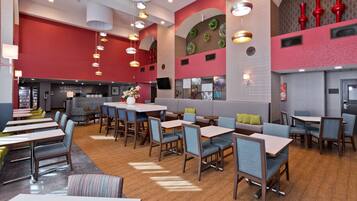 Un restaurant moderne doté de plusieurs espaces de restauration, notamment des banquettes et des tables, ainsi qu’un bar agrémenté d’une enseigne « Bienvenue ».