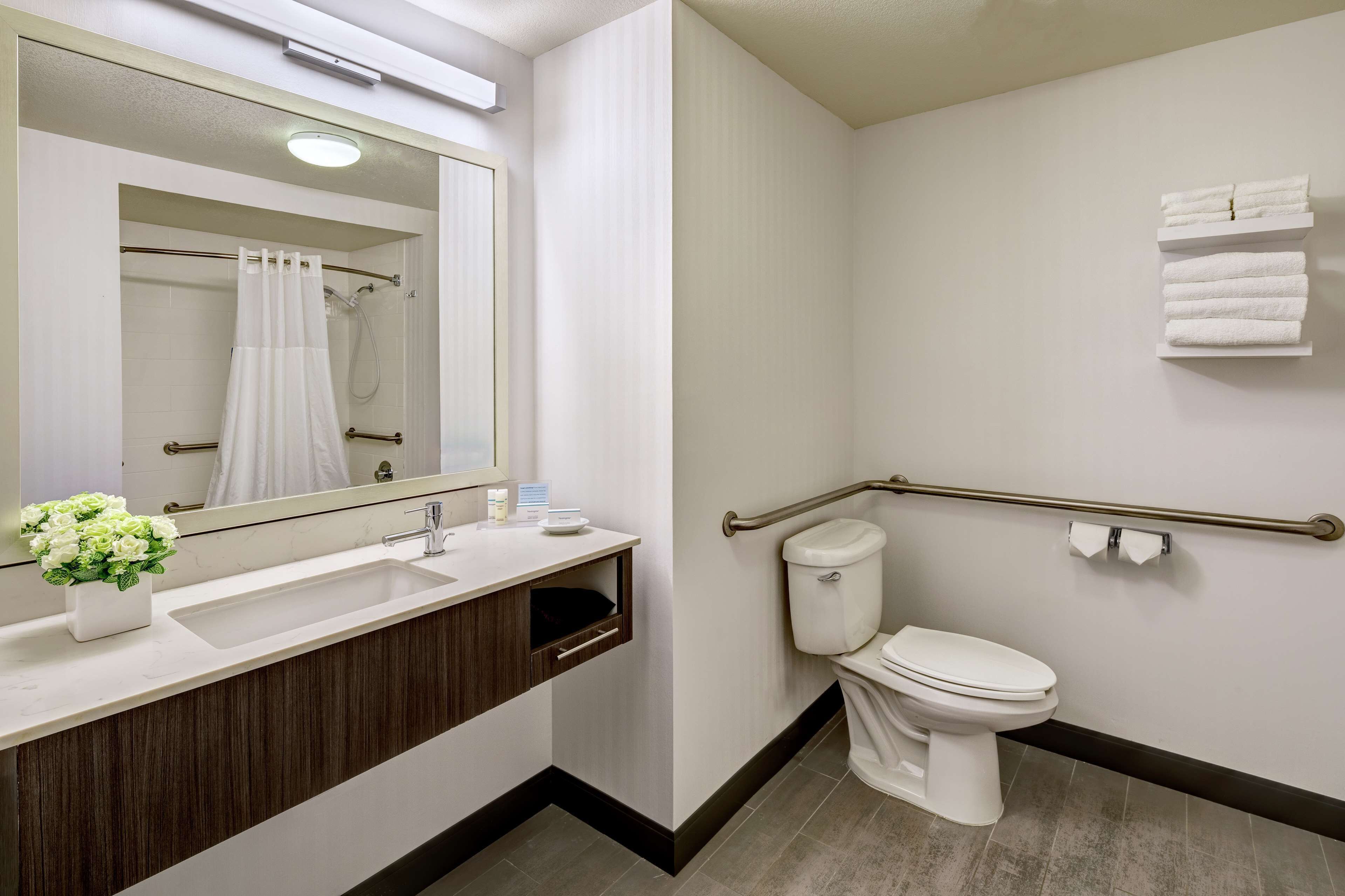 Un baño moderno con lavamanos, espejo, inodoro y barras de apoyo.