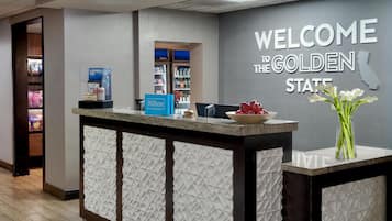 Mostrador de recepción de hotel con un letrero que dice 'Welcome to the Golden State', un minibar y un jarrón de flores.