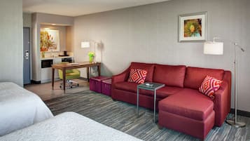 Una habitación de hotel con un sofá rojo, una mesita, un escritorio y una cama.