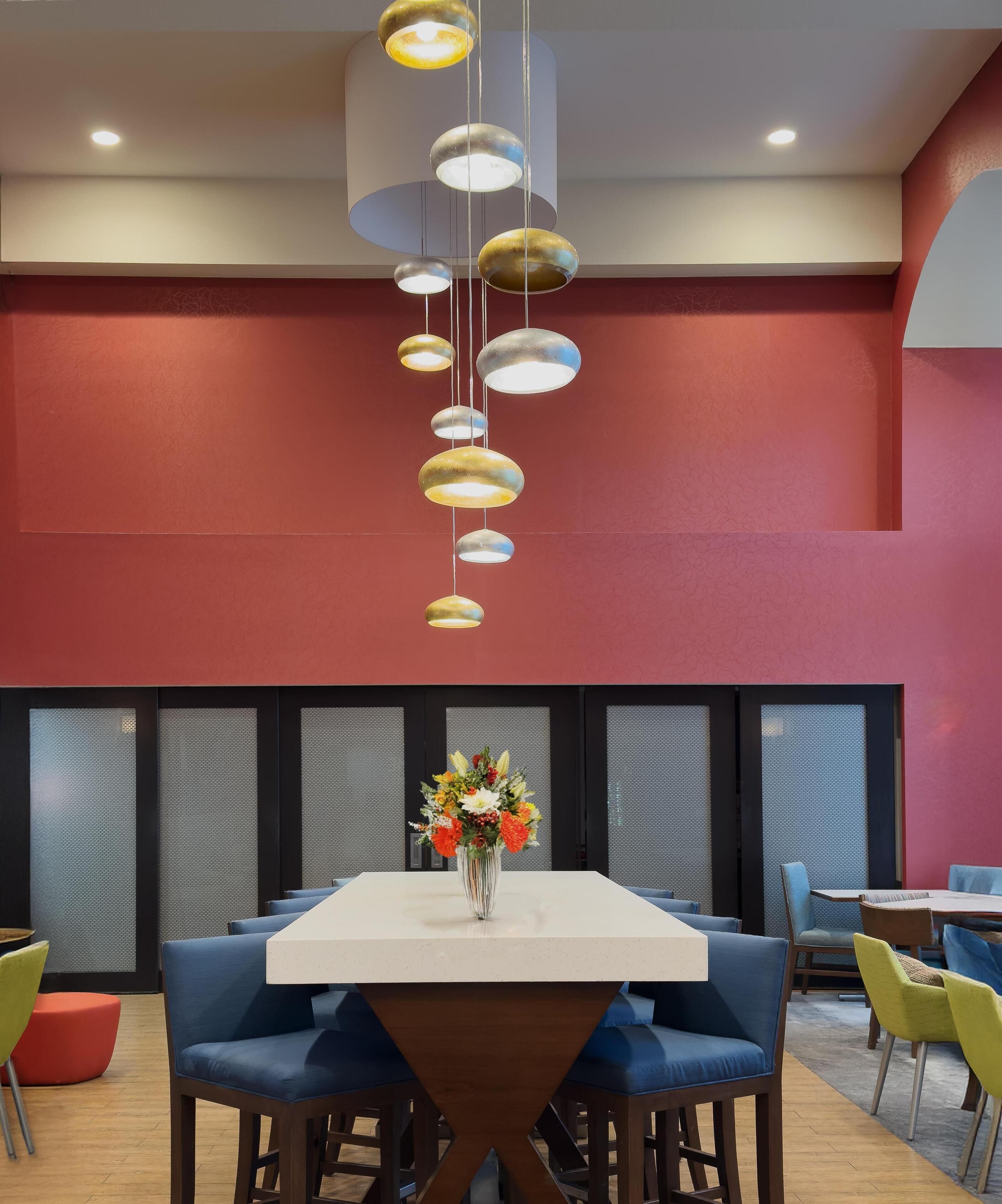 A modern dining area with a white table, blue upholstered chairs, and a hanging light fixture with multiple shades.