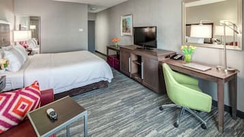 A hotel room with a bed, desk, chair, TV, and a mirror.