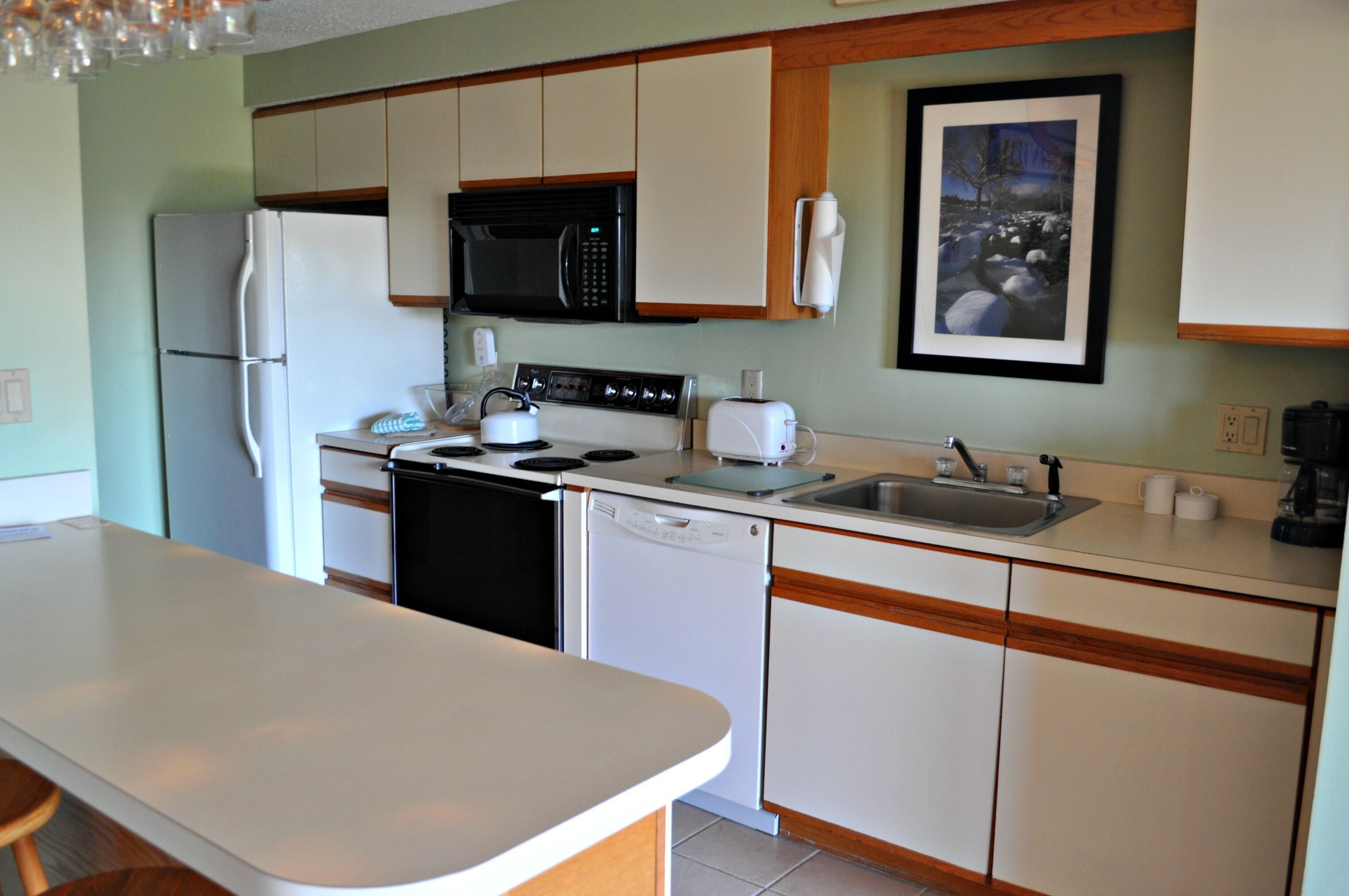 A kitchen with white cabinets, a black microwave, a white refrigerator, a dishwasher, a toaster, and a sink.