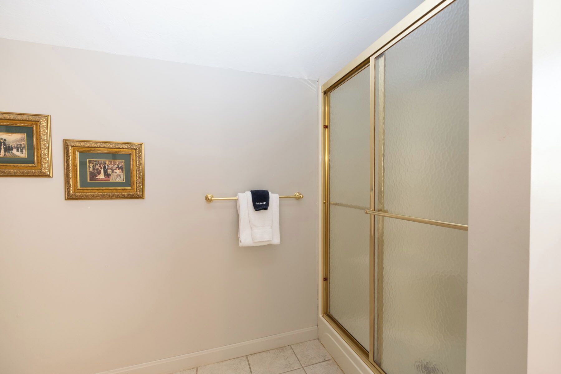 A bathroom with a glass shower door, a towel rack with a white towel, and two framed pictures on the wall.