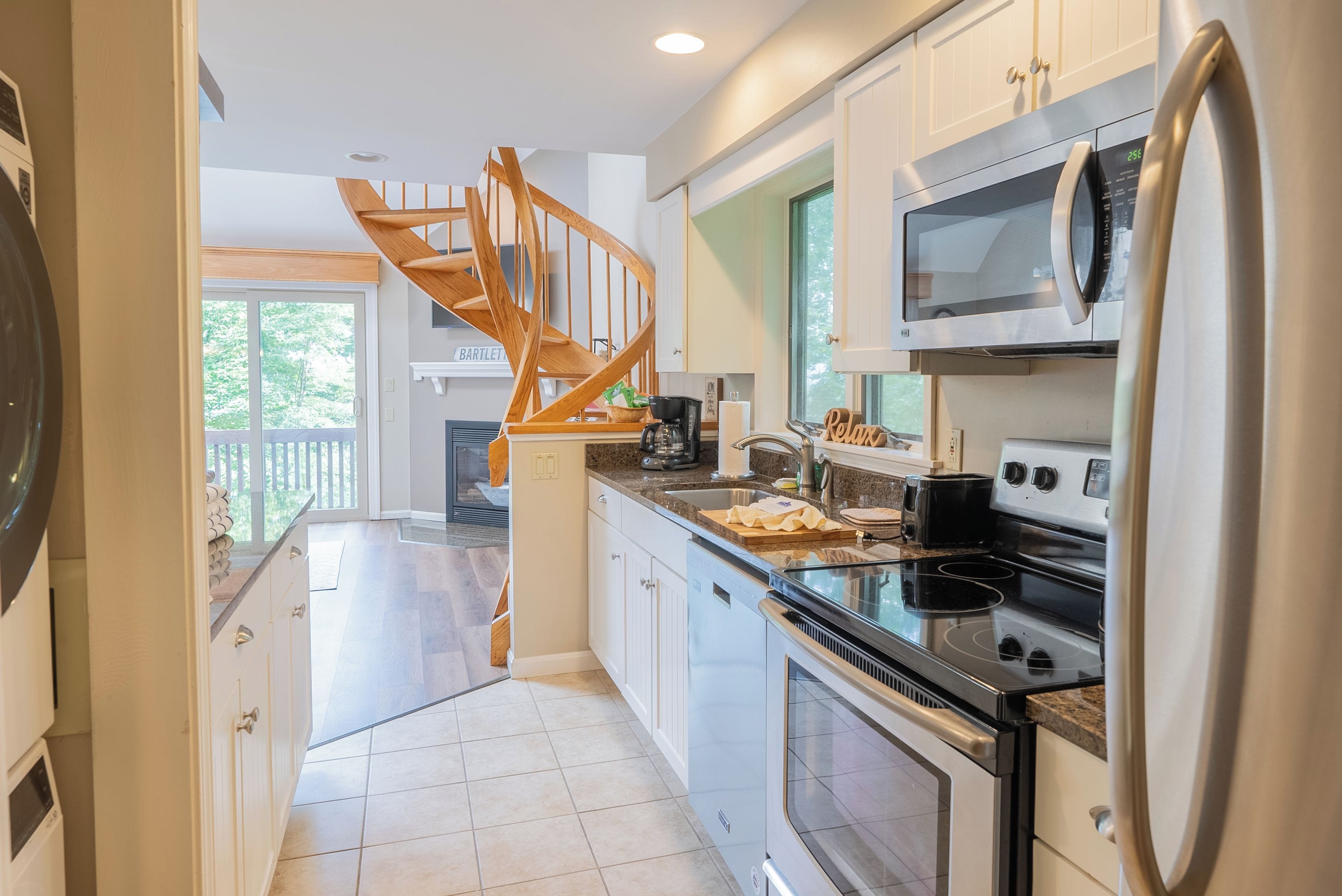 A modern kitchen with a wooden staircase, stainless steel appliances, and a view to the outside.