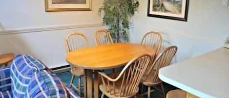A cozy room with a wooden dining table surrounded by chairs, a blue plaid sofa, and a small kitchen area with a white countertop.