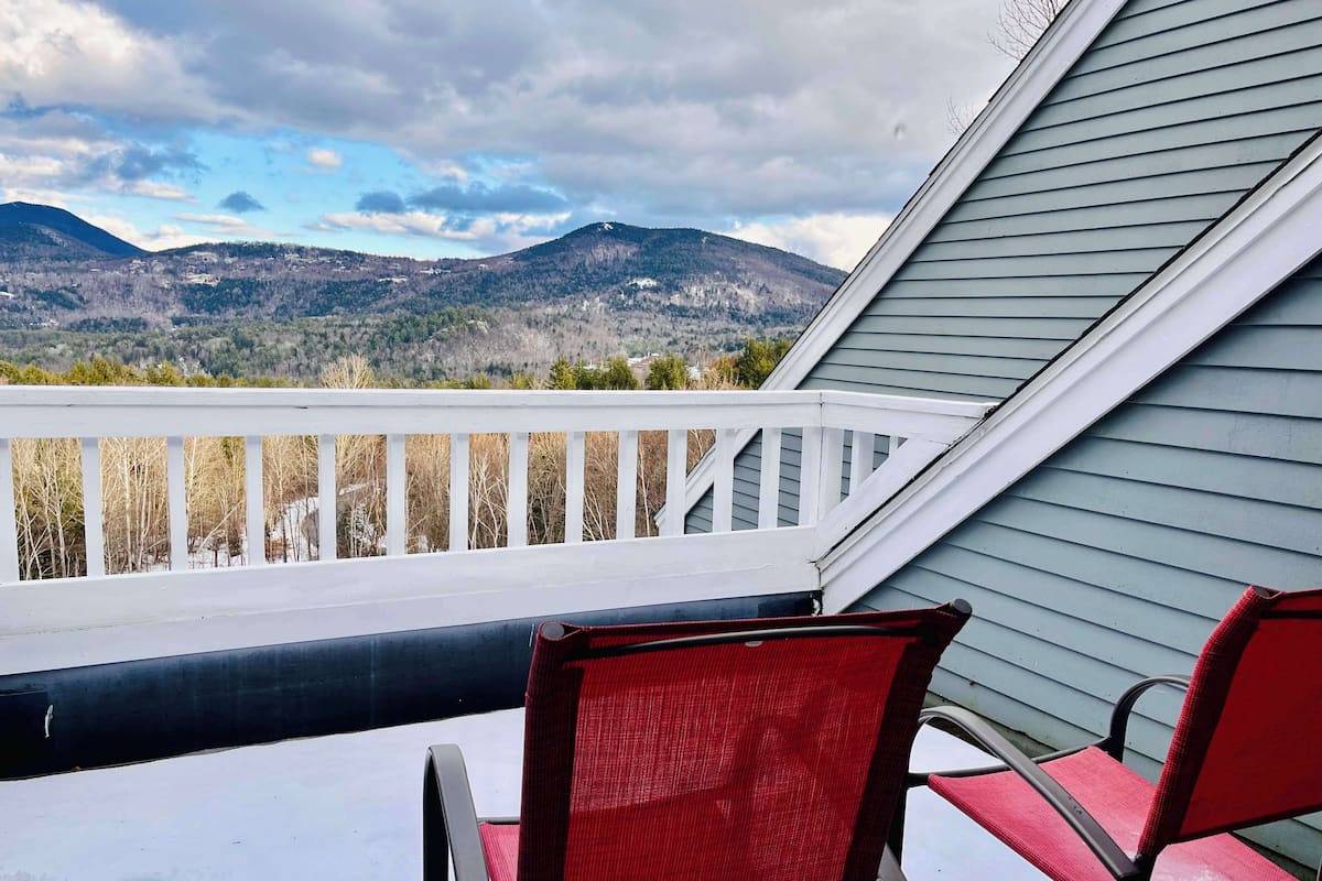 A balcony with a view of mountains, a railing, and two red chairs.