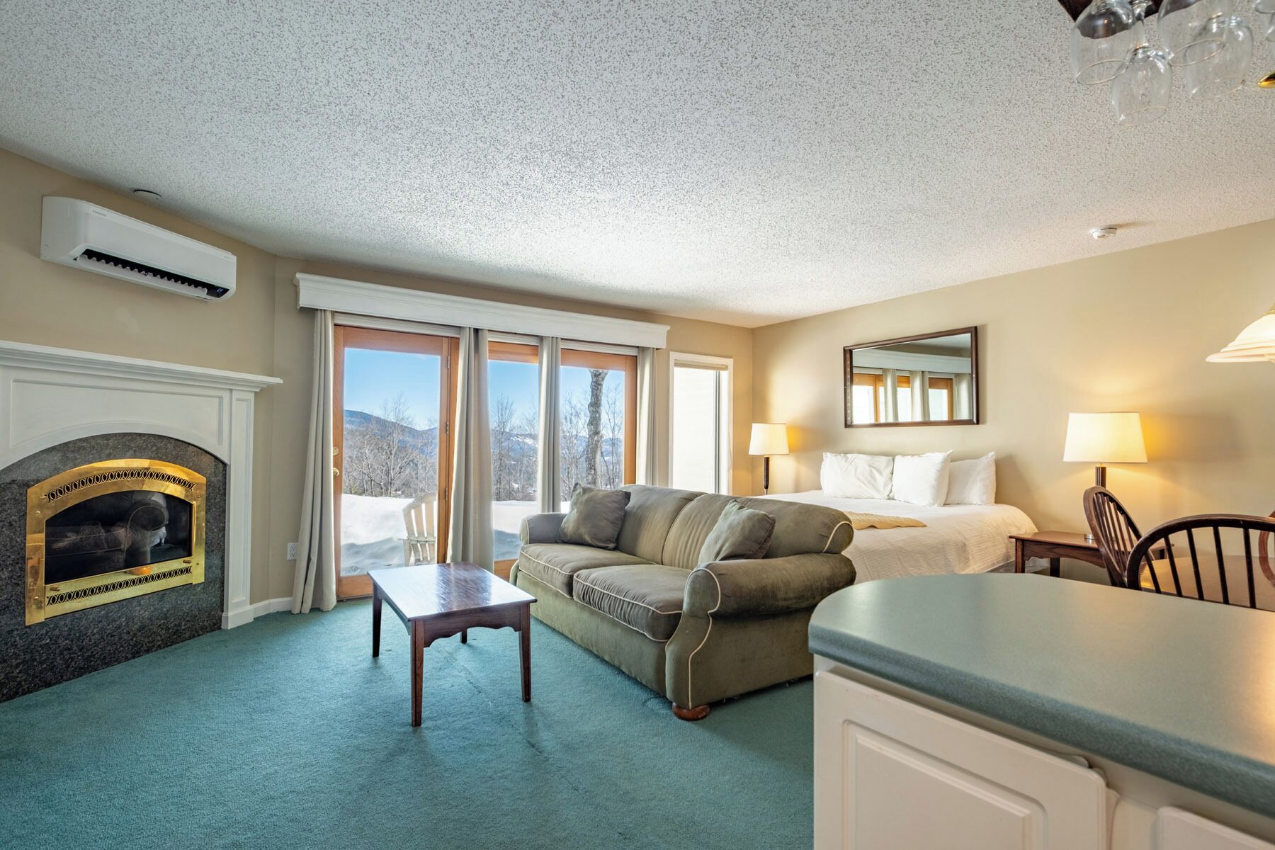 A hotel room with a fireplace, a sofa, a bed, a dining table, and a view of the outdoors.