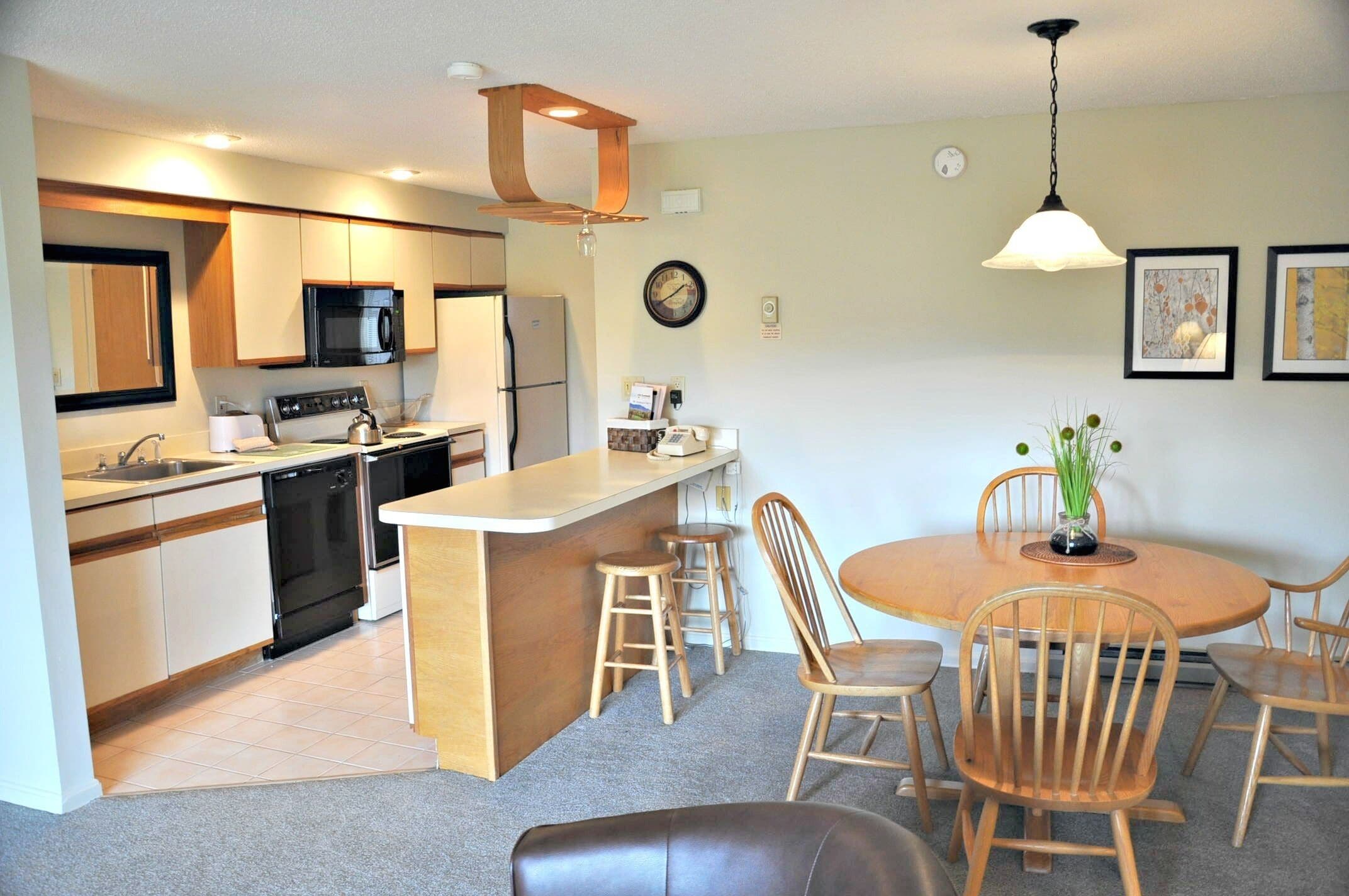 A compact kitchen with a central island, a dining area with wooden chairs, and a small table.