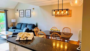 A modern kitchen with a dining area, featuring a kitchen island, wooden chairs, and a table with a neon sign. - Nordic Village Resort (Jackson)