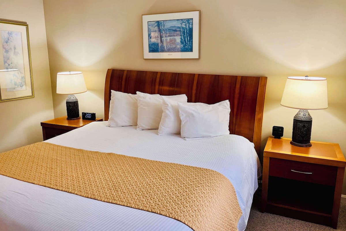 A neatly made bed with a wooden headboard, two bedside tables with lamps, and a framed picture on the wall.