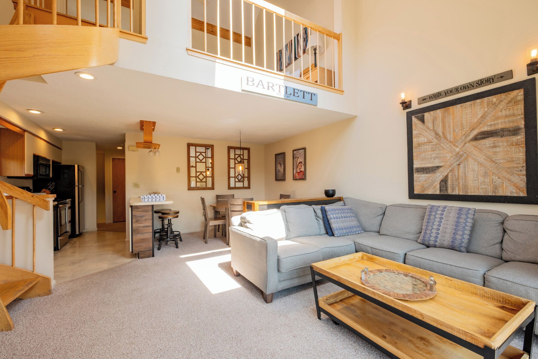 A spacious living area with a high ceiling, a staircase, a kitchen, and a dining area.