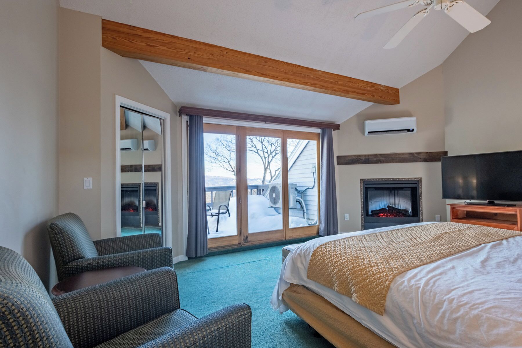 Habitación de hotel con cama, televisor, chimenea y puerta corrediza de vidrio que da a un balcón.