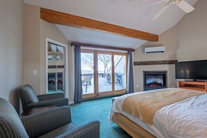 A hotel room with a bed, a television, a fireplace, and a sliding glass door leading to a balcony. - Nordic Village Resort (Jackson)