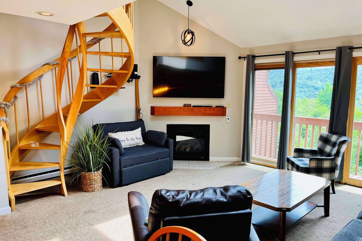 A modern living room with a spiral staircase, a flat-screen TV, a fireplace, and a balcony with a view.