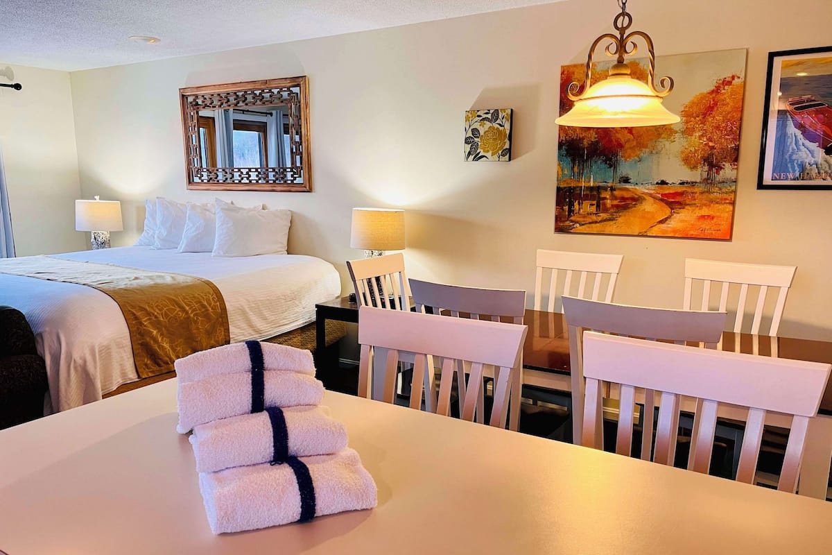 A hotel room with a bed, a dining table with chairs, a lamp, and artwork on the walls.