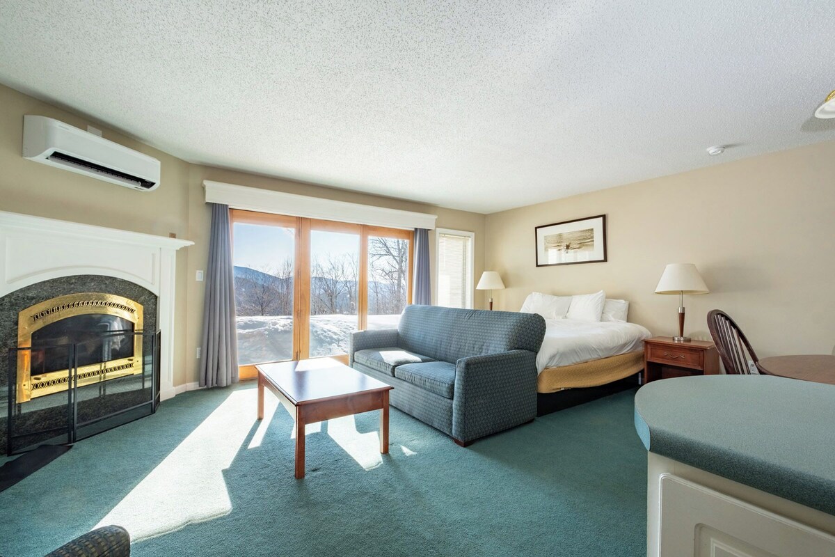 A hotel room with a fireplace, a sofa, a bed, and a desk.