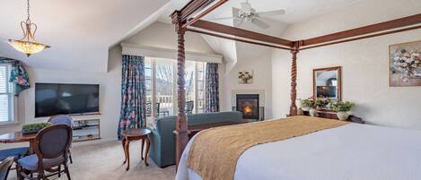 A spacious bedroom with a four-poster bed, a television, a desk with a chair, and a fireplace.