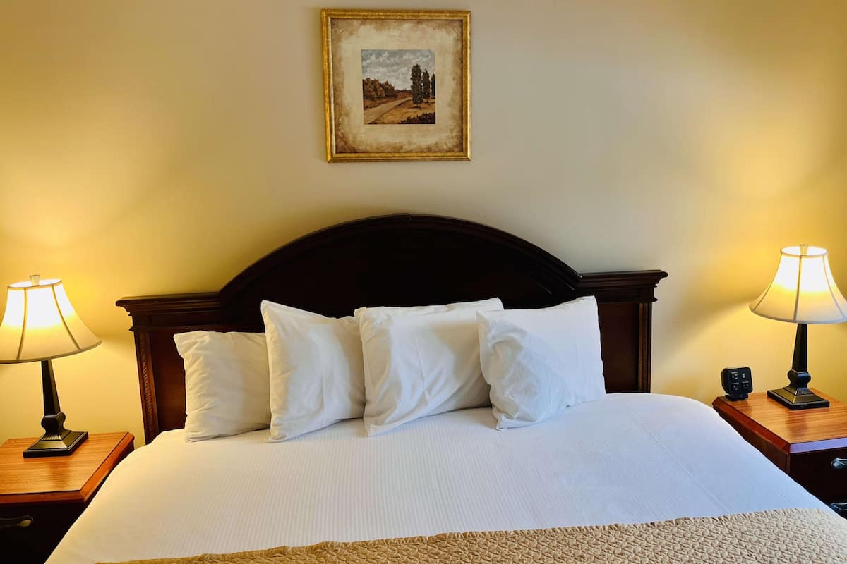 A neatly made bed with white linens and multiple pillows, flanked by two bedside tables with lamps, one of which has a remote control.