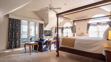 A four-poster bed with a canopy, a desk with a chair, a television, and a view of the outdoors through large windows.