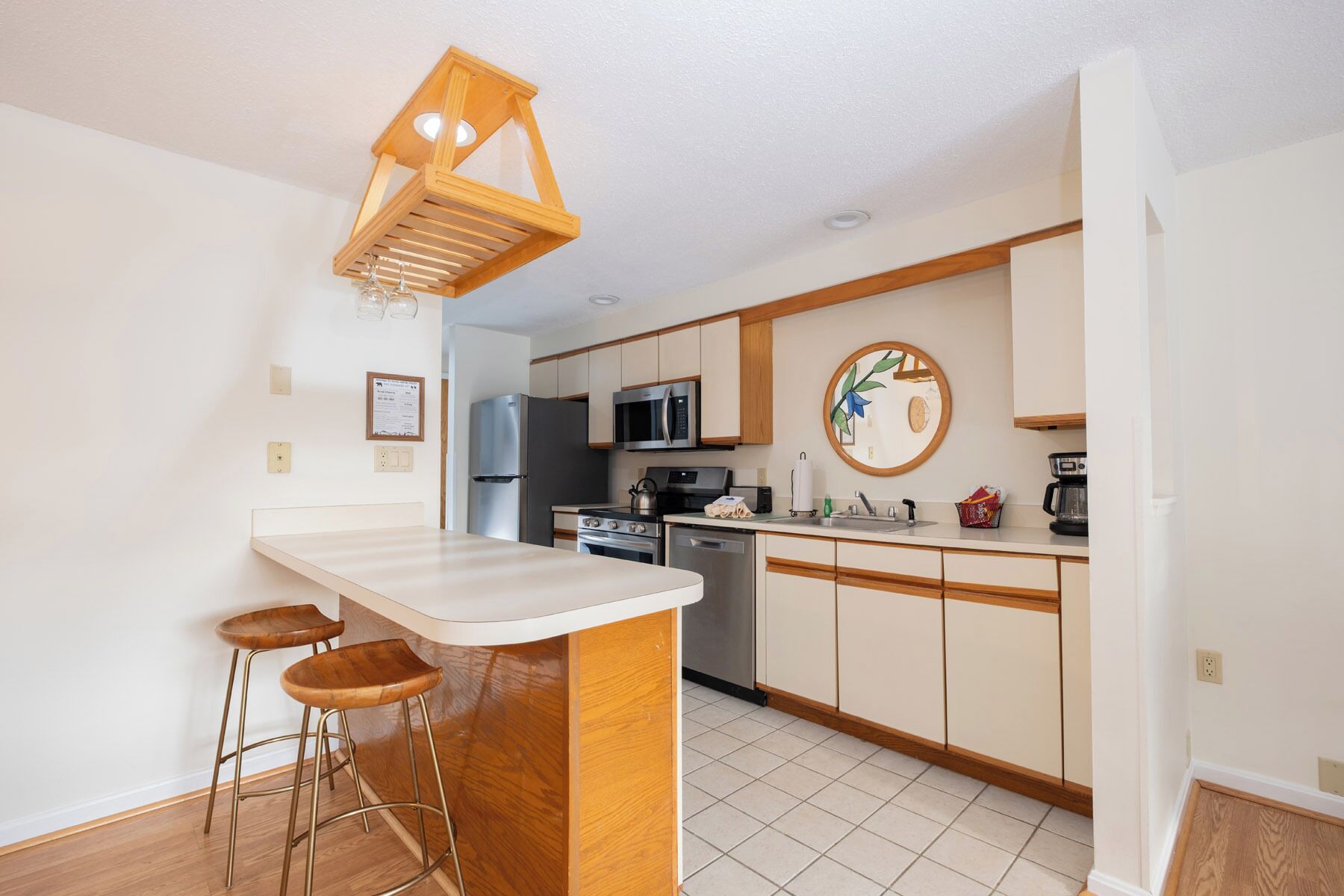 A modern kitchen with a central island, bar stools, stainless steel appliances, and a wooden ceiling light fixture.