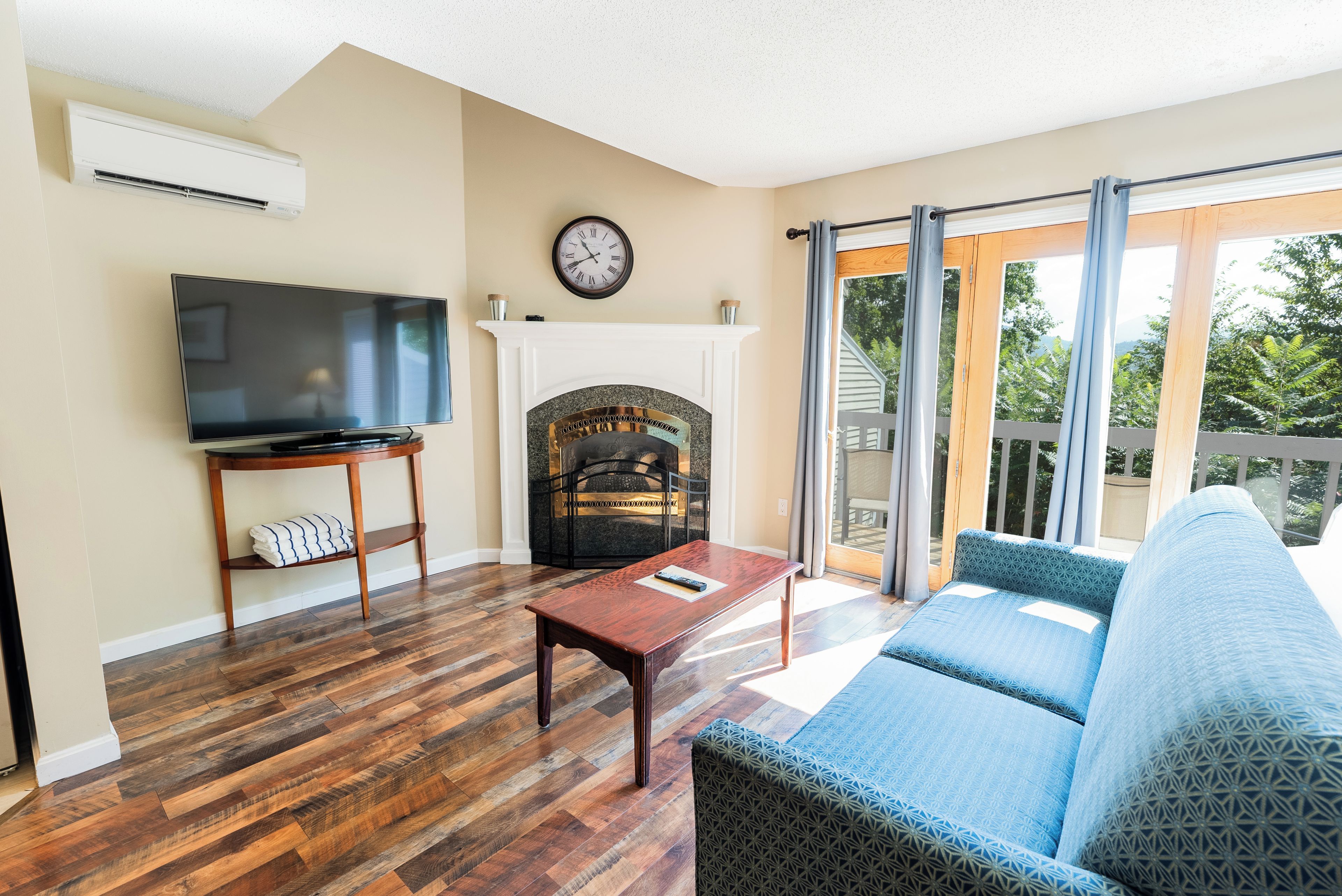 A living room with a flat-screen TV, a fireplace, a sofa, and a balcony with a view.