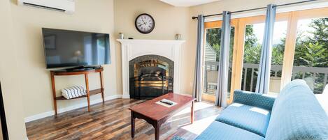 A living room with a flat-screen TV, a fireplace, a sofa, and a balcony with a view.