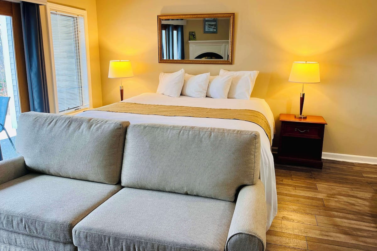 A hotel room with a bed, two bedside lamps, a sofa, a wooden floor, and a window with curtains.
