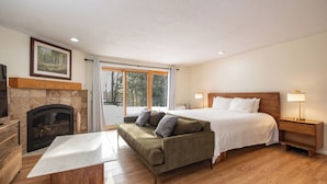 Un dormitorio con cama, sofá, mesita de noche, lámpara, chimenea y ventana grande.