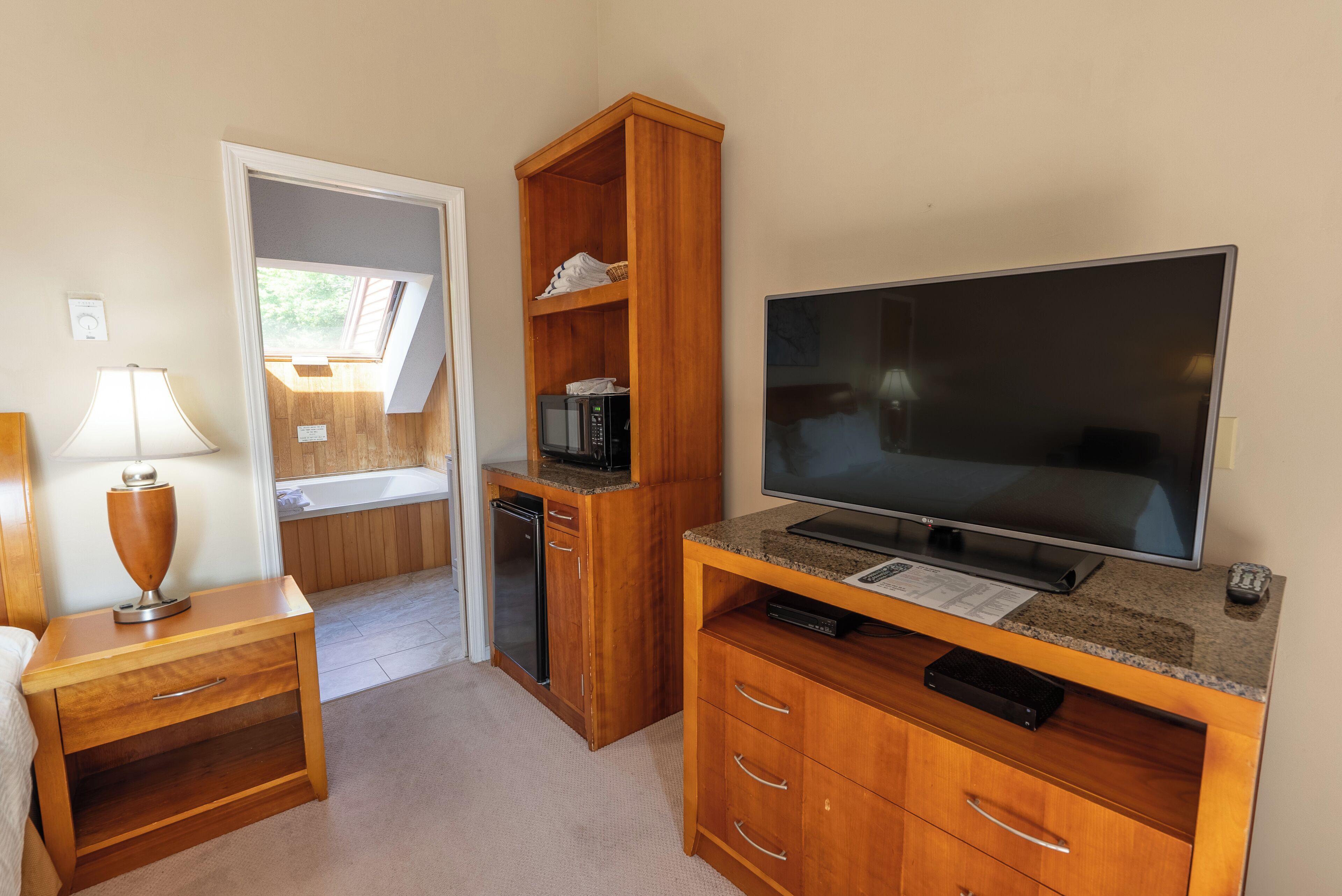 Een compacte kamer met een houten bureau, een flatscreen-tv, een magnetron en een klein kastje.
