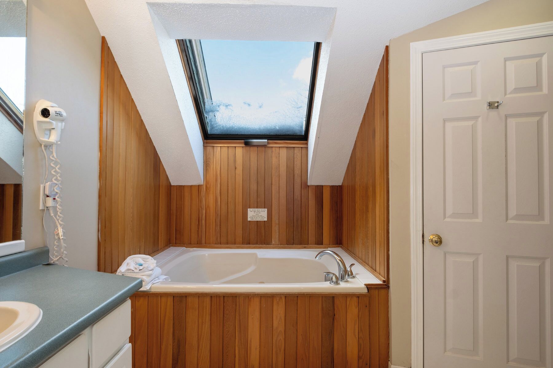 Une salle de bain avec un puits de lumière, un lambris en bois, une baignoire et une porte.