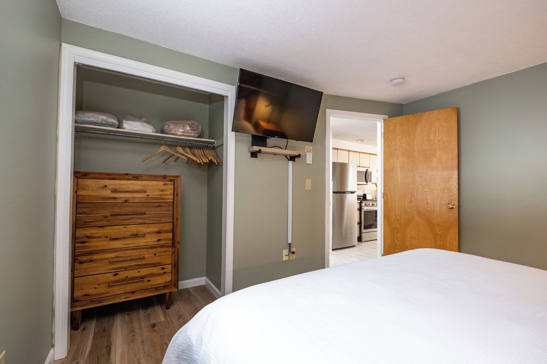 A bedroom with a wooden dresser, a bed, and a TV mounted on the wall.