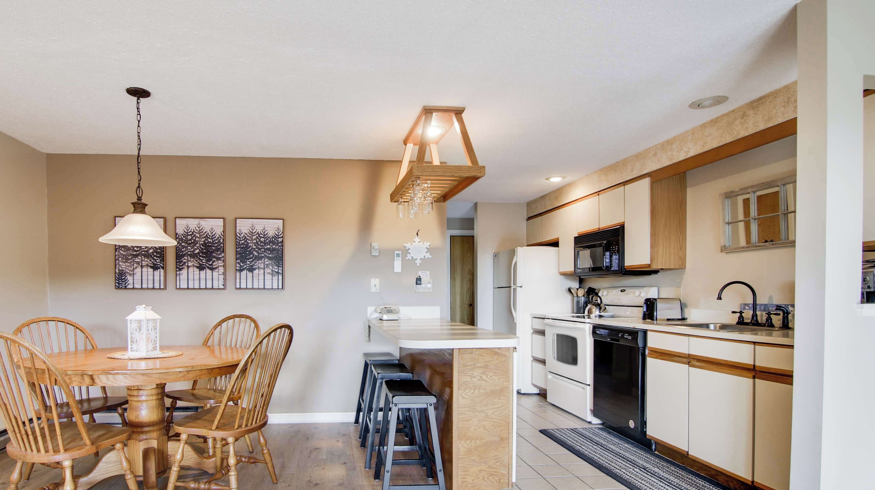 Una cocina moderna con una isla central, sillas de madera, una mesa de comedor y una lámpara colgante.