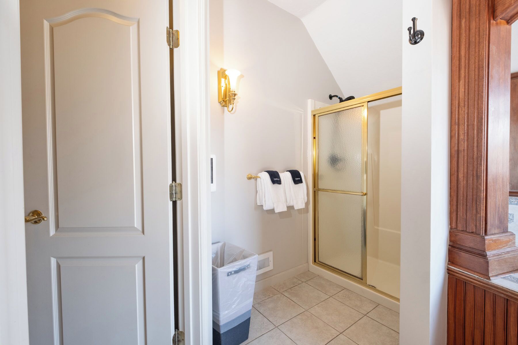 A bathroom with a shower, a towel rack with towels, and a trash bin.