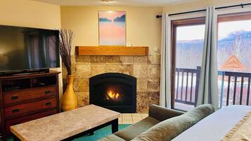 Una sala de estar con chimenea, televisor, sofá y vistas al exterior.