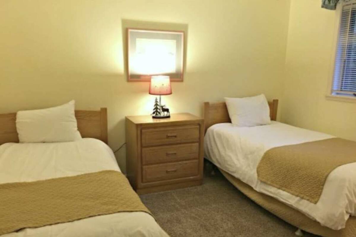 A room with two single beds, a nightstand with a lamp, and a framed picture on the wall.
